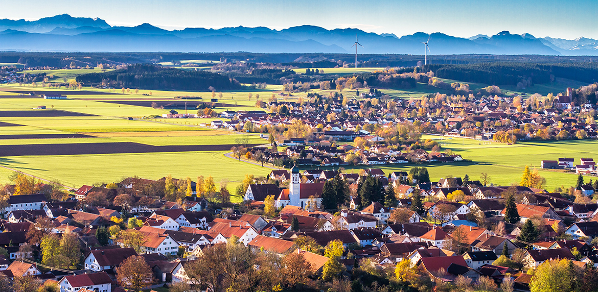 Foto einer bayerischen Kommune mit Windrädern vor einem Bergpanorama